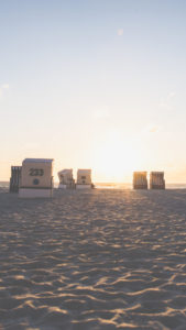 Beach chairs in the light of the sun setting in the sea, Sylt island, Germany, Europe