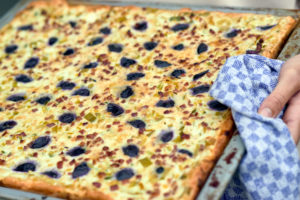 Quiche mit Trauben und Lauch im Backblech, gehalten von einer Frauenhand mit Küchentuch Quiche mit Trauben und Lauch im Backblech, gehalten von einer Frauenhand mit Küchentuch
