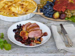 Entenbrust mit Trauben-Feigensoße, Gratin von Kartoffeln, Kürbis und Topinambur, Weintrauben und Feigen, Silberbesteck, Tisch mit unbehandelter Tischplatte Entenbrust mit Trauben-Feigensoße, Gratin von Kartoffeln, Kürbis und Topinambur, Weintrauben und Feigen, Silberbesteck, Tisch mit unbehandelter Tischplatte