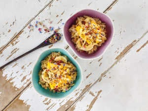 Ayurvedic cuisine - orange-apple-millet in colored bowls on a light wooden table top