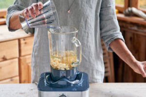 Steps to make almond milk, a woman adds more water to the mixture of almonds and maple syrup in a blender