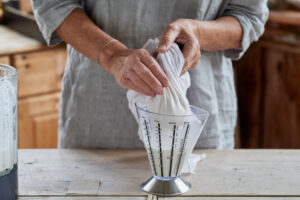 Steps for making almond milk, woman squeezing the crushed mass in the gauze cloth