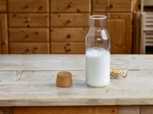 Steps for making almond milk, finished almond milk in a glass bottle with cork and a glass bowl with blanched almonds on a wooden table