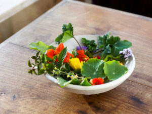 Bowl with edible flowers and herbs on a wooden table