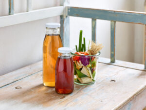 ayurvedic cuisine, two glass bottles filled with vegetable stock with cut vegetables on a wooden bench
