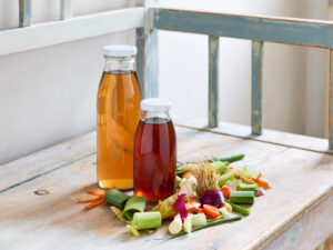 ayurvedic cuisine, two glass bottles filled with vegetable stock with cut vegetables on a wooden bench