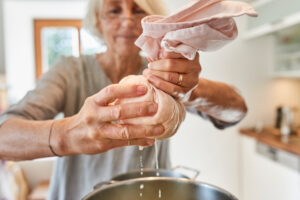 Making paneer, woman squeezing a cheesecloth filled with cream cheese and separating cheese from whey