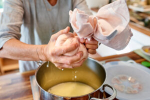 Making paneer, woman squeezing a cheesecloth filled with cream cheese and separating cheese from whey