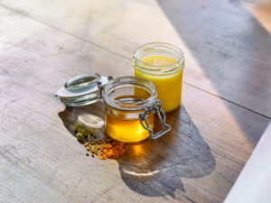 ayurvedic cuisine, one jar each with still liquid and already solid ghee, next to it turmeric powder, fenugreek seeds and cardamom