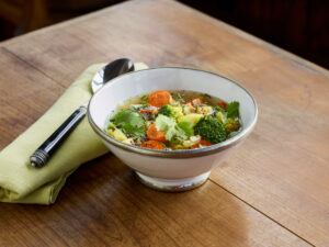 ayurvedic cuisine, vegetable soup in white bowl with silver rim on wooden table