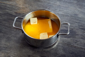 ayurvedic diet, steps to prepare homemade ghee from butter - organic sour cream butter in a stainless steel saucepan while melting, on a dark wooden table top.