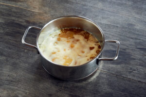 ayurvedic diet, steps to prepare homemade ghee from butter - melted sour cream butter in a stainless steel saucepan with egg white settling, on a dark wooden tabletop