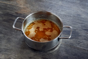 ayurvedic diet, steps to prepare homemade ghee from butter - melted sour cream butter in a stainless steel saucepan on a dark wooden table top, the ghee clarifies