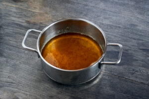 ayurvedic diet, steps to prepare homemade ghee from butter - melted sour cream butter in a stainless steel saucepan on a dark wooden table top, the ghee is clarified, sediments at the bottom of the saucepan