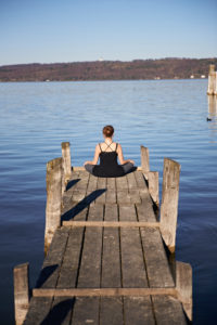 Meditation at the Ammersee, woman sitting on jetty, blue sky Meditation at the Ammersee, woman sitting on jetty, blue sky