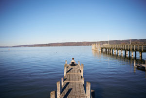 Meditation at the Ammersee, woman sitting on jetty, blue sky Meditation at the Ammersee, woman sitting on jetty, blue sky