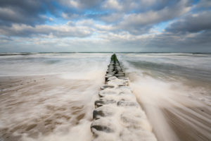 A beach on the Baltic Sea in winter, pulling waves, sea foam and groyne leading into the sea, long exposure A beach on the Baltic Sea in winter, pulling waves, sea foam and groyne leading into the sea, long exposure