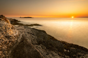 Evening light with sunset on the shores of the Mediterranean Sea on Cape Kamenjak in Istria, Croatia. Rugged rocks, long exposure to smooth water and a small island with clouds like a volcano in the background. Evening light with sunset on the shores of the Mediterranean Sea on Cape Kamenjak in Istria, Croatia. Rugged rocks, long exposure to smooth water and a small island with clouds like a volcano in the background.