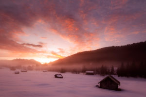 Sunrise in the Bavarian Alps near Garmisch-Partenkirchen. In the background the Sowendgruppe of the Karwendel and fantastic colors, in the foreground classic haystacks and morning mist, in snow and cold. Sunrise in the Bavarian Alps near Garmisch-Partenkirchen. In the background the Sowendgruppe of the Karwendel and fantastic colors, in the foreground classic haystacks and morning mist, in snow and cold.