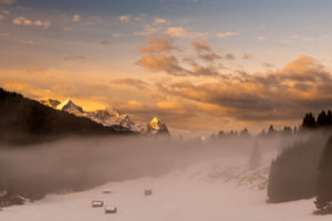 Zugspitze, Alpspitze und Wettersteingebirge am frühen Morgen. Im Vordergrund einige kleine Heuschober, Holzhütten und Nebel, während das Morgenrot die Schnee Landschaft in warme orangetöne taucht. Zugspitze, Alpspitze und Wettersteingebirge am frühen Morgen. Im Vordergrund einige kleine Heuschober, Holzhütten und Nebel, während das Morgenrot die Schnee Landschaft in warme orangetöne taucht.