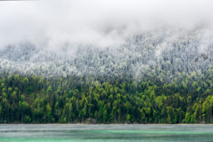 Shore of the Eibsee during the Eisheiligen. Turquoise blue water, green forest, fresh snow and thick clouds divide this picture into four areas. Shore of the Eibsee during the Eisheiligen. Turquoise blue water, green forest, fresh snow and thick clouds divide this picture into four areas.