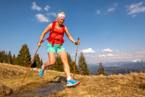 Trail runner jumps over a small stream on a mountain meadow, in the background the German Alps and blue sky. Trail runner jumps over a small stream on a mountain meadow, in the background the German Alps and blue sky.