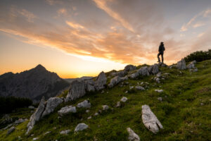 Climbers on a rock formation in the morning red on the Kompar in the Karwendel. In the background the Mondscheinspitze and a great morning red / sky colors. The summit of Mondscheinspitze clearly stands out, while the silhouette of the man stands out against the sky.