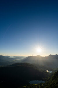 Sun star over Karwendel, Ferchensee and Lautersee, as well as the forested Kranzberg in Werdenfelser Land, on the border with Tyrol/Austria. The two small lakes lie in the dense and dark forest, while in the background the sun rises over the Karwendel.
