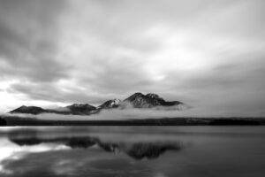 Dense clouds and fog at the Walchensee, the Herzogstand and Heimgarten are reflected in the clear water of the Alpen See.