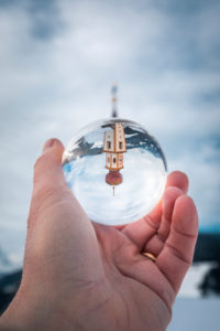 The alpine church of St. Georg in Pliscia / Plaiken in winter seen through a crystal ball, municipality of Marebbe / Enneberg, Bolzano, Alto Adige, Südtirol, Italy