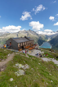 Hikers at Olperer refuge with Lake Schlegeispeicher on the background, Zillertal Alps, Tyrol, Schwaz district, Austria Hikers at Olperer refuge with Lake Schlegeispeicher on the background, Zillertal Alps, Tyrol, Schwaz district, Austria
