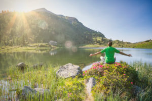man 40 - 50 years old in relaxing position at sunrise on the shore of the Colbricon alpine lake in summer with rhododendron flowering and mountain reflected on the water, Lagorai, Trentino, Italy, Europe man 40 - 50 years old in relaxing position at sunrise on the shore of the Colbricon alpine lake in summer with rhododendron flowering and mountain reflected on the water, Lagorai, Trentino, Italy, Europe