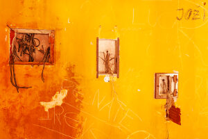 Weathered orange wall of an abandoned building with graffiti and hanging electric wires, showing signs of urban decay