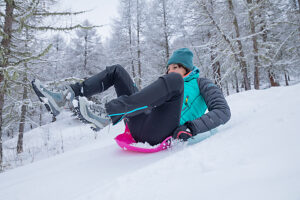 Woman, 45 years old, enjoying a fun winter day, sledding on fresh snow in colorful sportswear