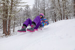 Teen girl sledding on fresh snow, laughing and enjoying a fun winter day in bright sportswear