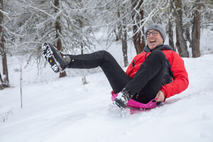 Mature man sledding on snow with colorful sportswear, enjoying a winter day of fun and excitement