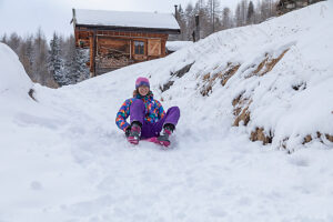 Teen girl sledding on fresh snow, laughing and enjoying a fun winter day in bright sportswear