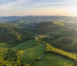 Aerial view of green rolling hills, cultivated fields, and a farmhouse in the rural landscape of Cesane Park during spring, near Urbino, Marche region, central Italy