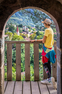 A young hiker looks out from the arched entrance of the Powder Tower (Pulverturm), along the scenic Tappeiner Promenade above Merano. South Tyrol, Trentino-Alto Adige, northern Italy