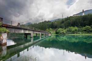 Old concrete bridge over Lake Centro Cadore with the bell tower of Domegge di Cadore parish church in the background. Belluno province, Veneto, Italy