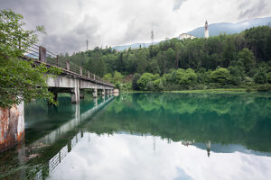 Old concrete bridge over Lake Centro Cadore with the bell tower of Domegge di Cadore parish church in the background. Belluno province, Veneto, Italy