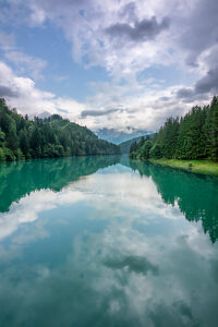 Centro Cadore Lake after spring rain, with cloudy skies and forested Alpine peaks. Domegge di Cadore, Belluno province, Veneto, northern Italy