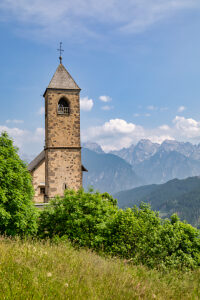 The Church of San Leonardo Vecchio, a unique Gothic-medieval architectural gem built in the mid-1500s by Nicolo Roupel, stands peacefully in Casamazzagno, Comelico Superiore, with the Dolomites towering in the background ñ Belluno Province, Veneto, Italy