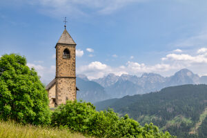 The Church of San Leonardo Vecchio, a unique Gothic-medieval architectural gem built in the mid-1500s by Nicolo Roupel, stands peacefully in Casamazzagno, Comelico Superiore, with the Dolomites towering in the background ñ Belluno Province, Veneto, Italy