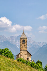 The Church of San Leonardo Vecchio, a unique Gothic-medieval architectural gem built in the mid-1500s by Nicolo Roupel, stands peacefully in Casamazzagno, Comelico Superiore, with the Dolomites towering in the background ñ Belluno Province, Veneto, Italy