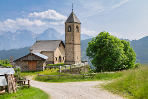 The Church of San Leonardo Vecchio, a unique Gothic-medieval architectural gem built in the mid-1500s by Nicolo Roupel, stands peacefully in Casamazzagno, Comelico Superiore, with the Dolomites towering in the background ñ Belluno Province, Veneto, Italy