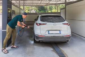 A man washing his SUV/crossover with a high-pressure jet at a self-service coin-operated car wash A man washing his SUV/crossover with a high-pressure jet at a self-service coin-operated car wash