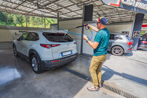 A man washing his SUV/crossover with a high-pressure jet at a self-service coin-operated car wash A man washing his SUV/crossover with a high-pressure jet at a self-service coin-operated car wash