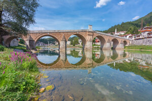 Stara Cuprija (Old Bridge), historic Ottoman stone bridge spanning the Neretva River, reflected in clear waters with vibrant purple flowers in the foreground. National monument and landmark of Balkan heritage. Konjic, Herzegovina-Neretva Canton, Bosnia and Herzegovina Stara Cuprija (Old Bridge), historic Ottoman stone bridge spanning the Neretva River, reflected in clear waters with vibrant purple flowers in the foreground. National monument and landmark of Balkan heritage. Konjic, Herzegovina-Neretva Canton, Bosnia and Herzegovina