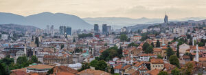 Panoramic view of Sarajevo with red rooftops, historic mosques, modern skyscrapers, and surrounding mountains at sunset. Sarajevo, Bosnia and Herzegovina Panoramic view of Sarajevo with red rooftops, historic mosques, modern skyscrapers, and surrounding mountains at sunset. Sarajevo, Bosnia and Herzegovina